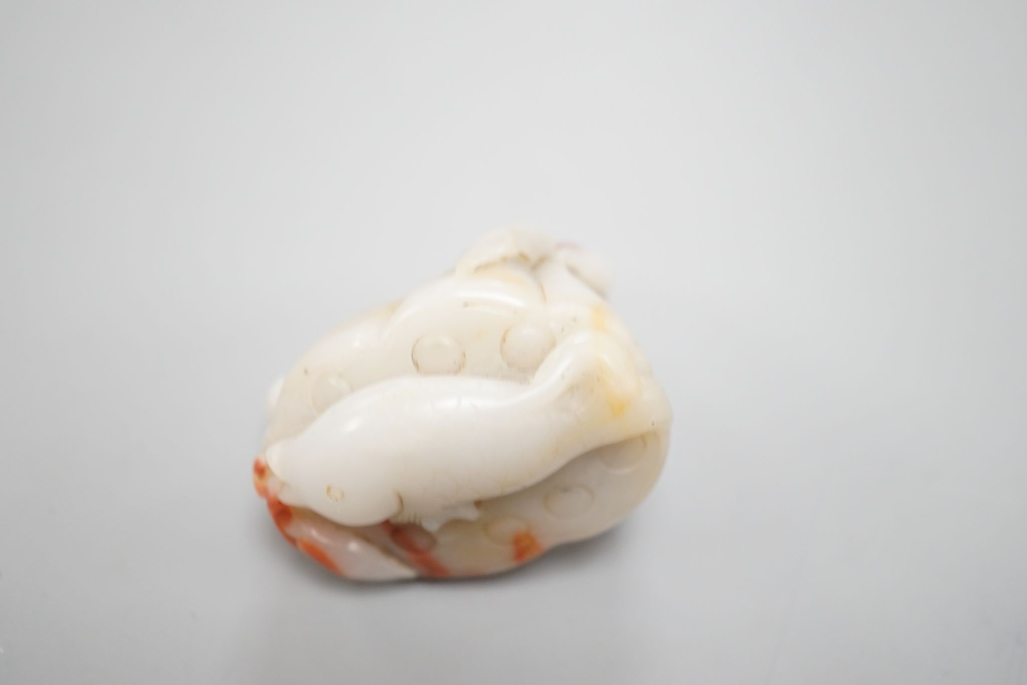 A Chinese pale celadon and russet jade 'lotus pod and fish' carving 6cm
